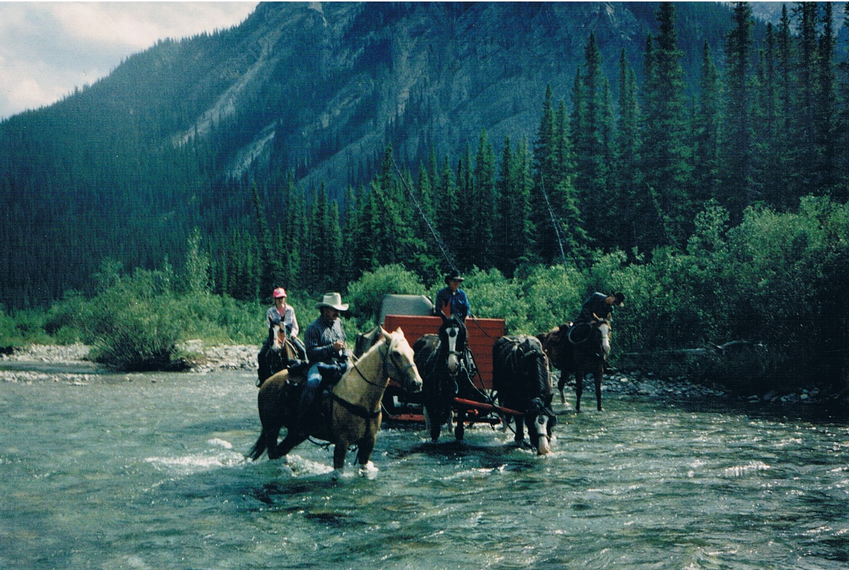 Riders and wagon crossing a river in the Alberta backcountry — Barrier Mountain Outfitters legacy